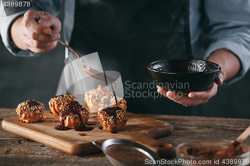 Image of Decorating delicious homemade eclairs with chocolate and peanuts