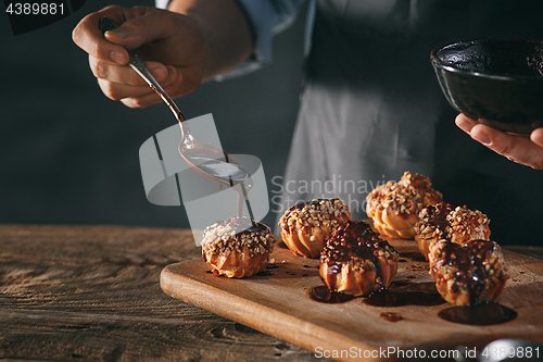 Image of Decorating delicious homemade eclairs with chocolate and peanuts