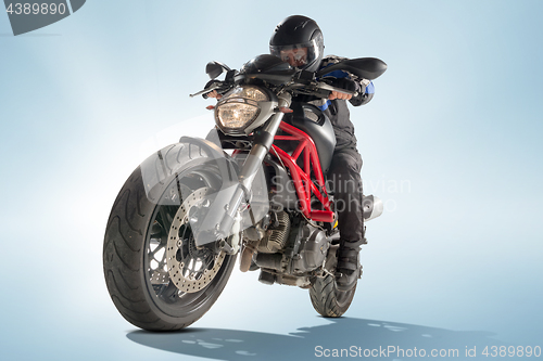 Image of Biker in black jacket and helmet sitting on his sportive bike on blue background