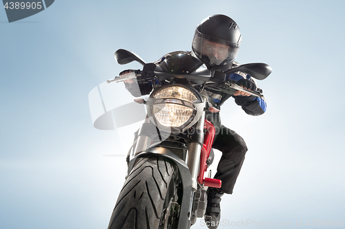 Image of Biker in black jacket and helmet sitting on his sportive bike on blue background