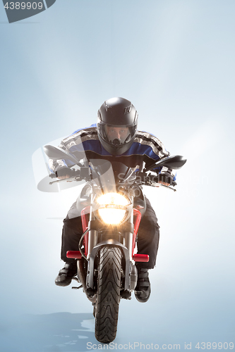 Image of Biker in black jacket and helmet sitting on his sportive bike on blue background