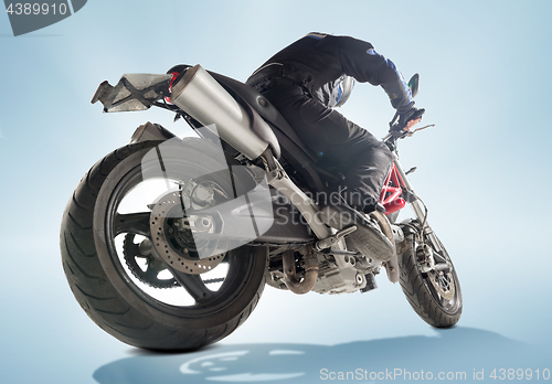 Image of Biker in black jacket and helmet sitting on his sportive bike on blue background