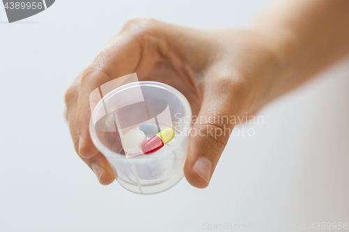 Image of close up of female hand with pills in medicine cup