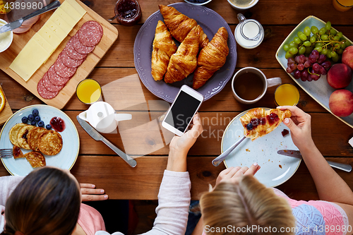 Image of women with smartphones eating food at table