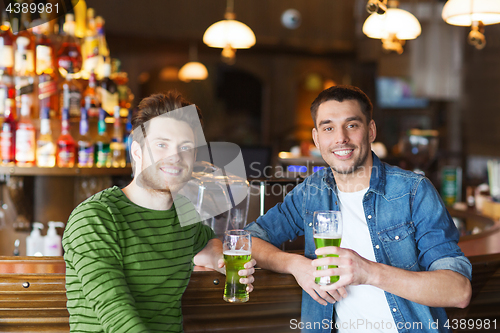 Image of male friends drinking green beer at bar or pub