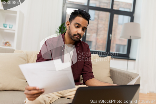 Image of upset man with laptop and papers at home