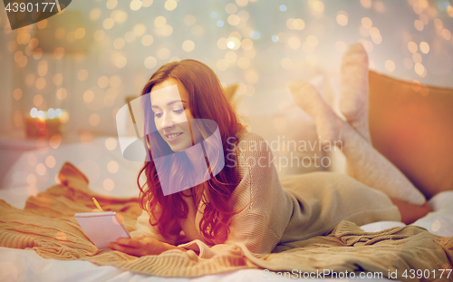 Image of happy young woman with notebook in bed at home