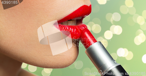 Image of close up of woman applying red lipstick to lips