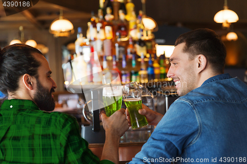 Image of male friends drinking green beer at bar or pub