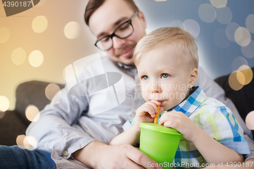 Image of father and son drinking from cup at home