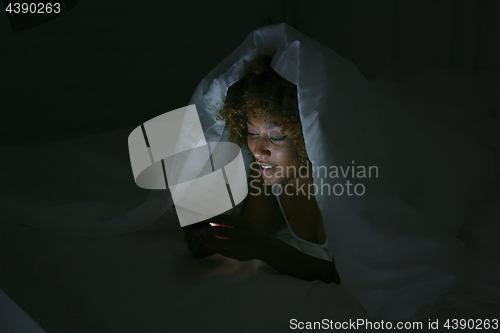 Image of Young woman using phone in dark room