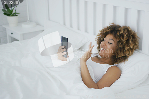 Image of Smiling woman in bed talking online