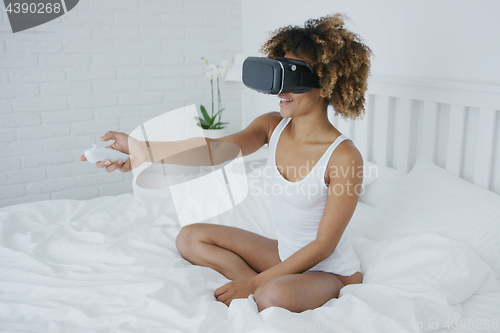 Image of Smiling woman in VR glasses on bed