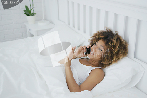 Image of Content woman talking on phone in bed