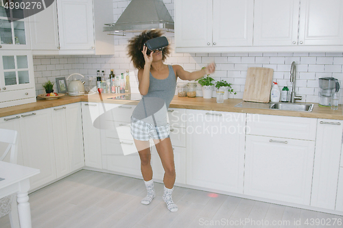 Image of Woman in VR glasses dancing in kitchen