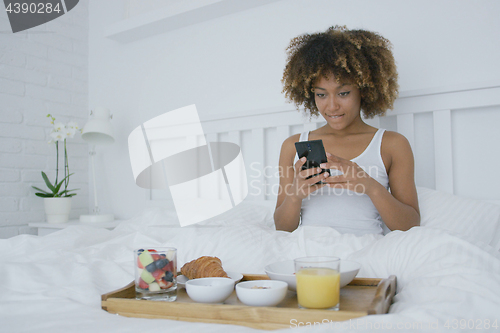 Image of Woman with smartphone in bed having meal