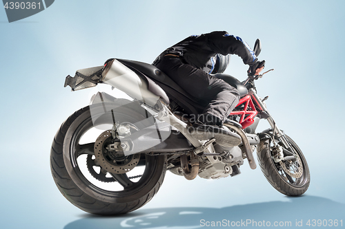 Image of Biker in black jacket and helmet sitting on his sportive bike on blue background