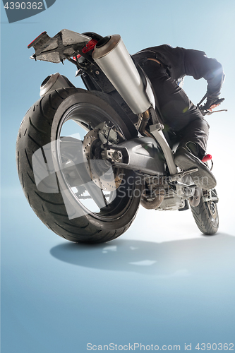 Image of Biker in black jacket and helmet sitting on his sportive bike on blue background