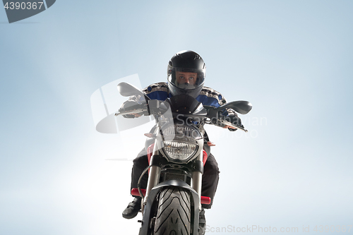 Image of Biker in black jacket and helmet sitting on his sportive bike on blue background