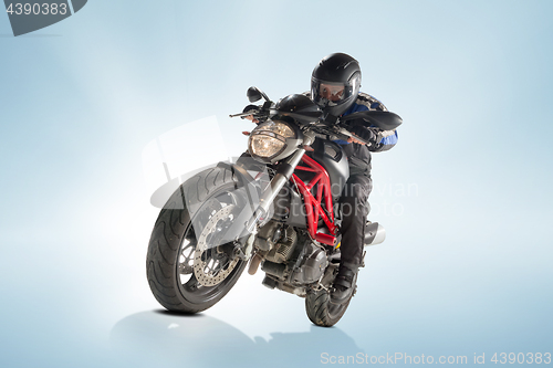 Image of Biker in black jacket and helmet sitting on his sportive bike on blue background