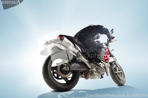 Image of Biker in black jacket and helmet sitting on his sportive bike on blue background