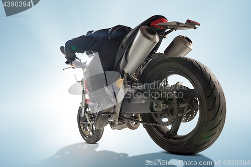 Image of Biker in black jacket and helmet sitting on his sportive bike on blue background