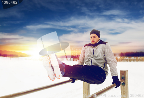 Image of young man exercising on parallel bars in winter