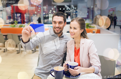 Image of happy couple with smartphone taking selfie in mall