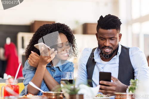 Image of happy man and woman with smartphones at restaurant