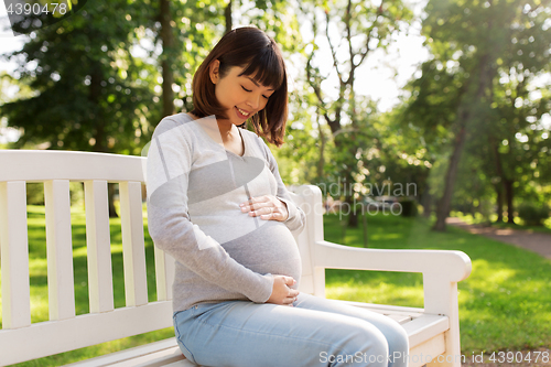 Image of happy pregnant asian woman sitting on park bench