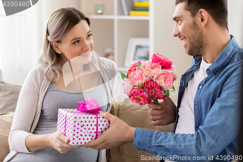 Image of man giving flowers to pregnant woman at home