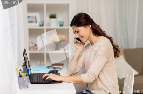 Image of woman with laptop calling on smartphone at home