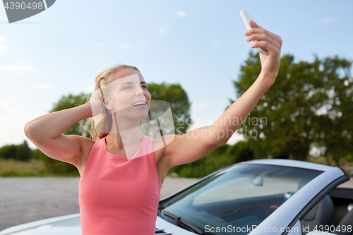 Image of woman posing at convertible car and taking selfie