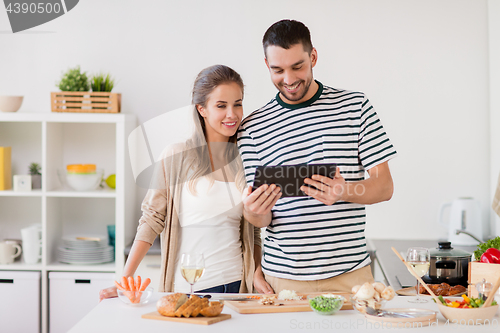 Image of happy couple with tablet pc cooking food at home