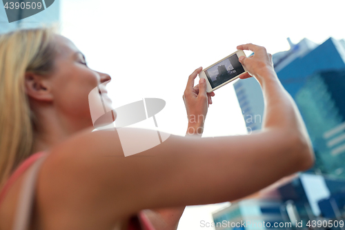 Image of young woman with smartphone photographing city