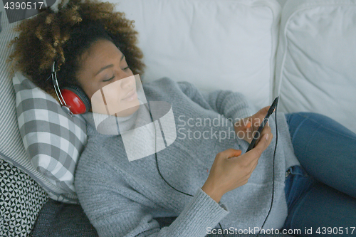 Image of Young woman chilling on sofa with gadgets