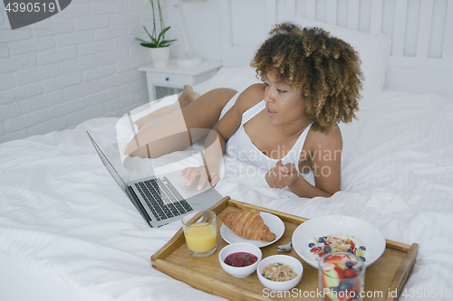 Image of Content woman using laptop while having meal