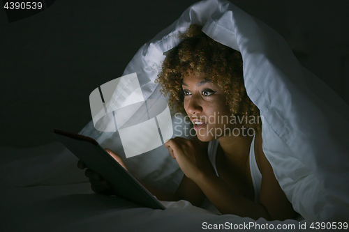 Image of Woman using tablet under blanket