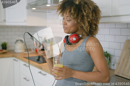 Image of Casual woman relaxing with phone in kitchen