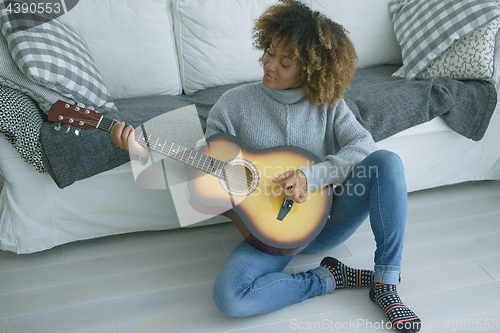 Image of Young woman playing guitar at home