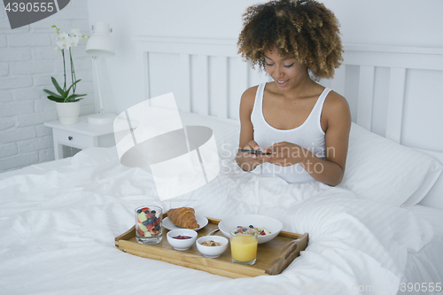 Image of Charming woman using phone while having breakfast