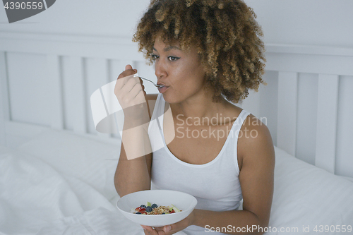 Image of Young woman eating breakfast in bed
