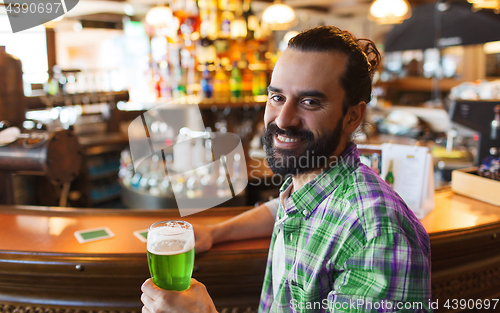 Image of man drinking green beer at bar or pub