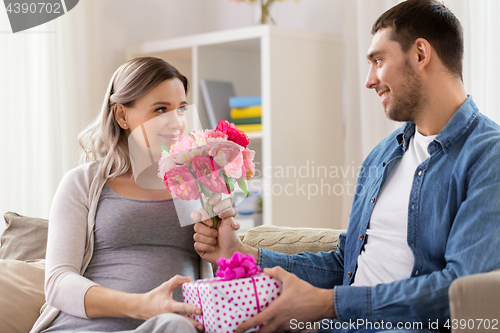 Image of man giving flowers to pregnant woman at home