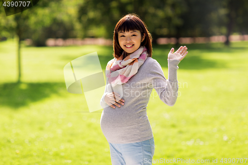 Image of happy pregnant asian woman waving hand at park