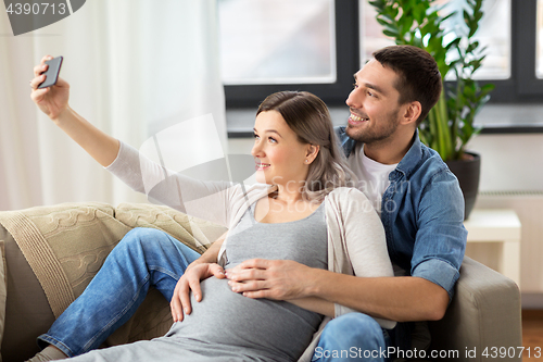 Image of man and pregnant woman taking selfie at home
