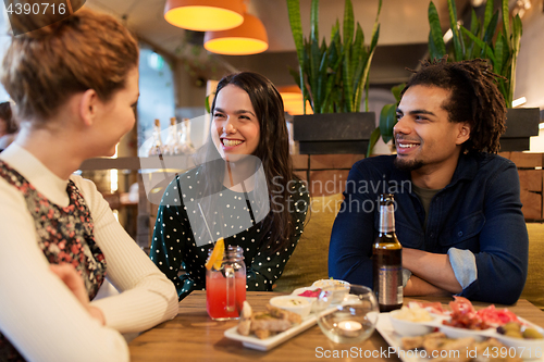 Image of happy friends with drinks and food at bar or cafe