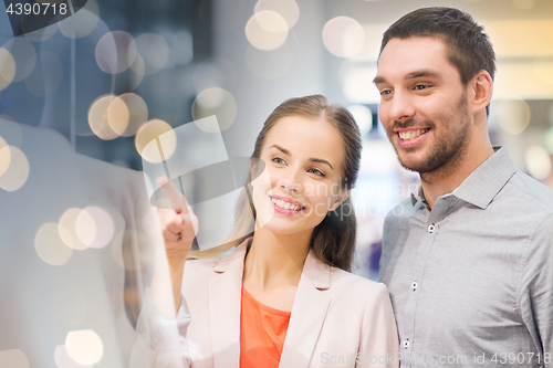 Image of happy couple pointing finger to shop window