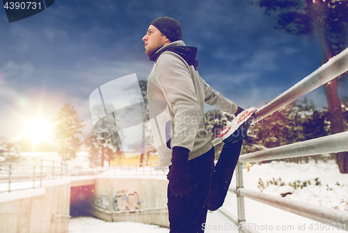 Image of sports man stretching leg at fence in winter