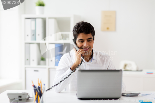 Image of happy businessman calling on desk phone at office